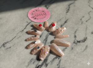 Set of decorative false nails with gemstones on a marble surface, branded 'ARIA'.