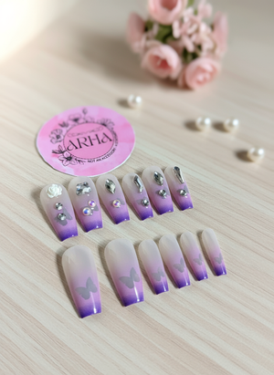 Set of gradient purple and white nail art designs with decorative elements on a wooden surface, featuring a 'ARHA' brand sticker.