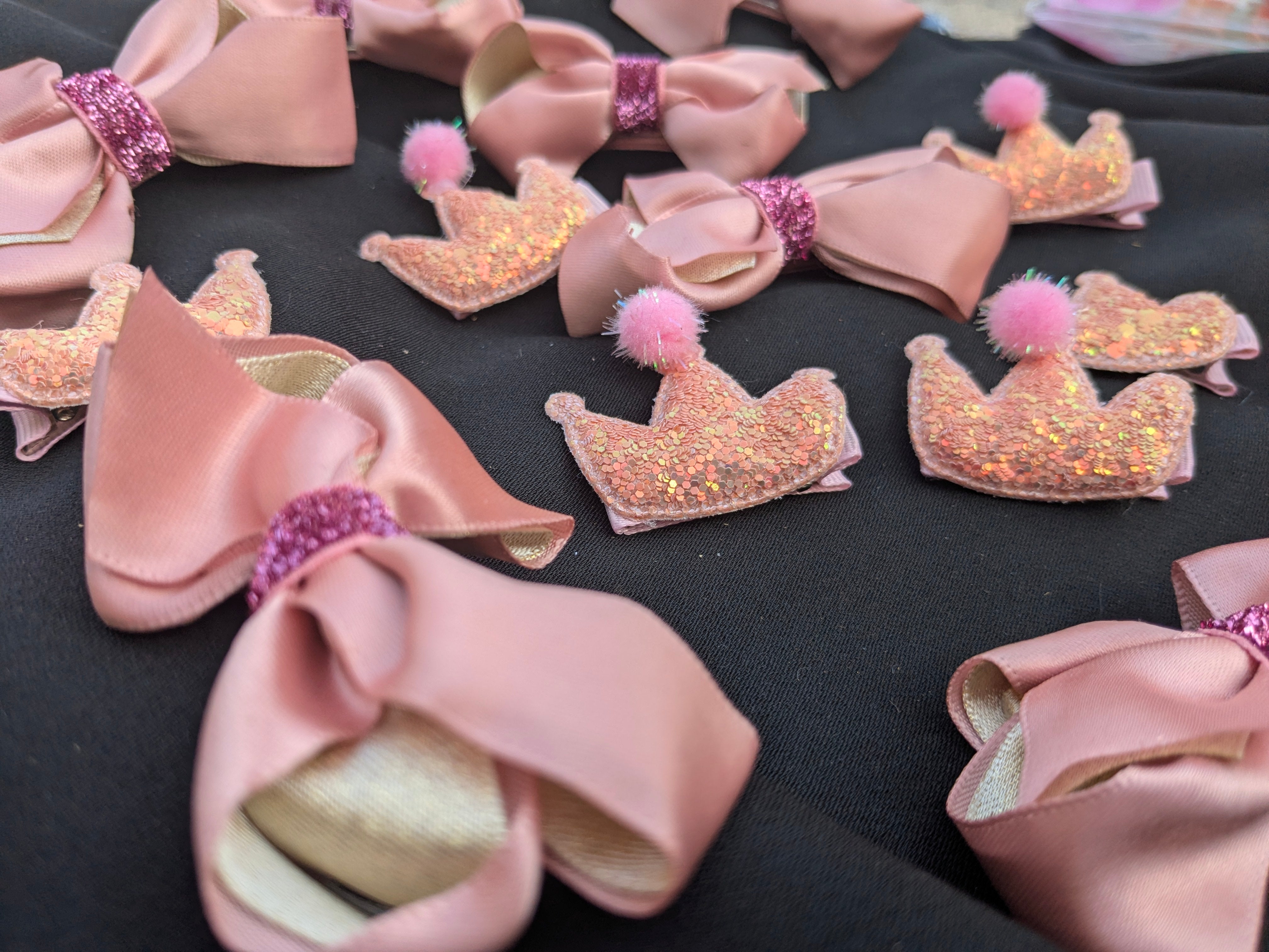 Pink bows with glittery crowns and pom-poms on a black surface