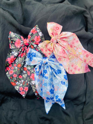 Elegant blush pink floral hair bow made of premium satin fabric, featuring a delicate wildflower meadow print for a romantic hairstyle."