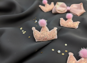 crowns with pink pom-poms hair pins on a dark fabric background