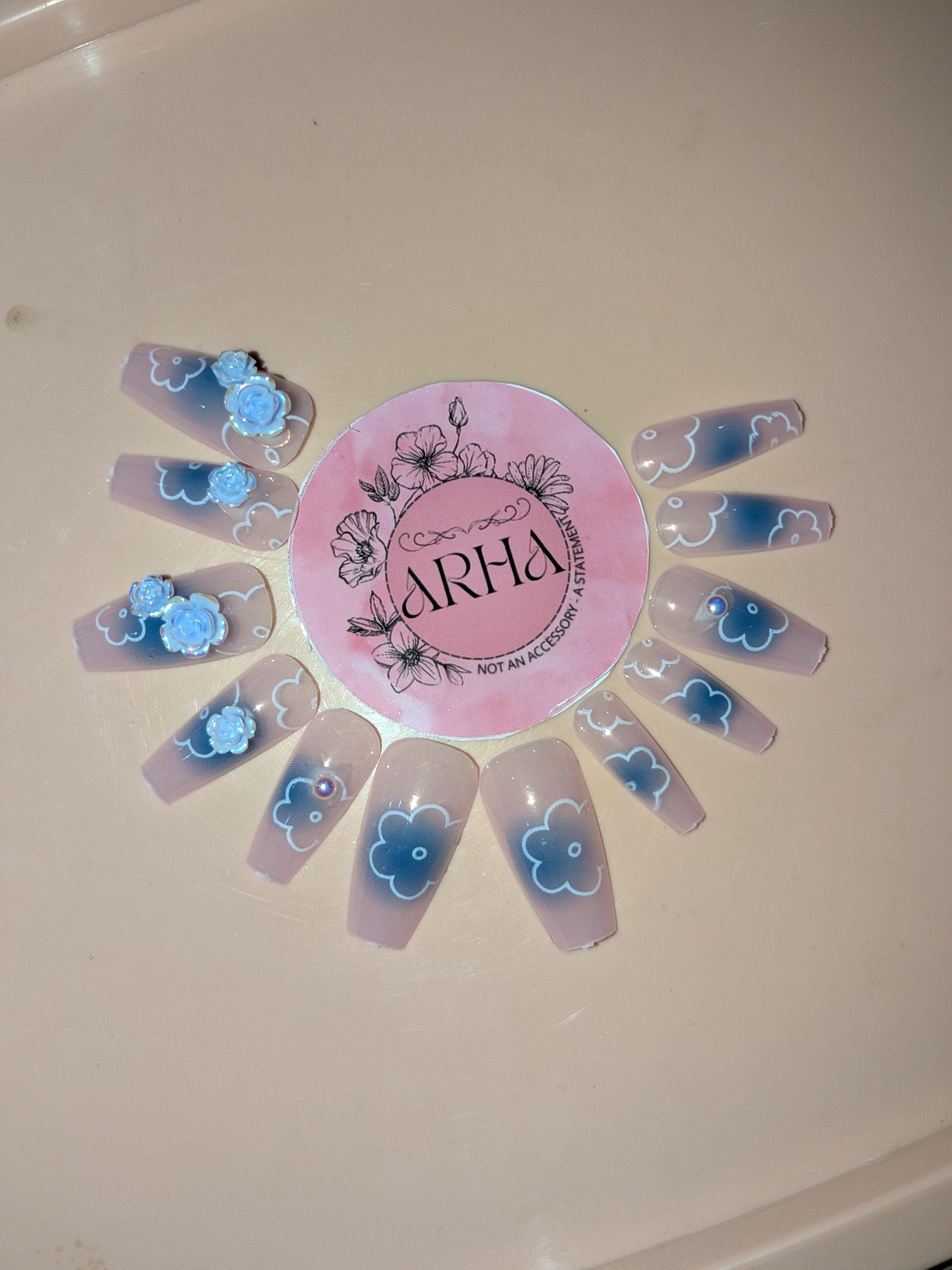 Nail art display with blue floral designs on clear nail sheets and a pink 'ARHA' logo.