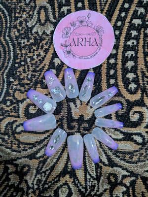 Set of purple and white nail extensions on a patterned fabric background