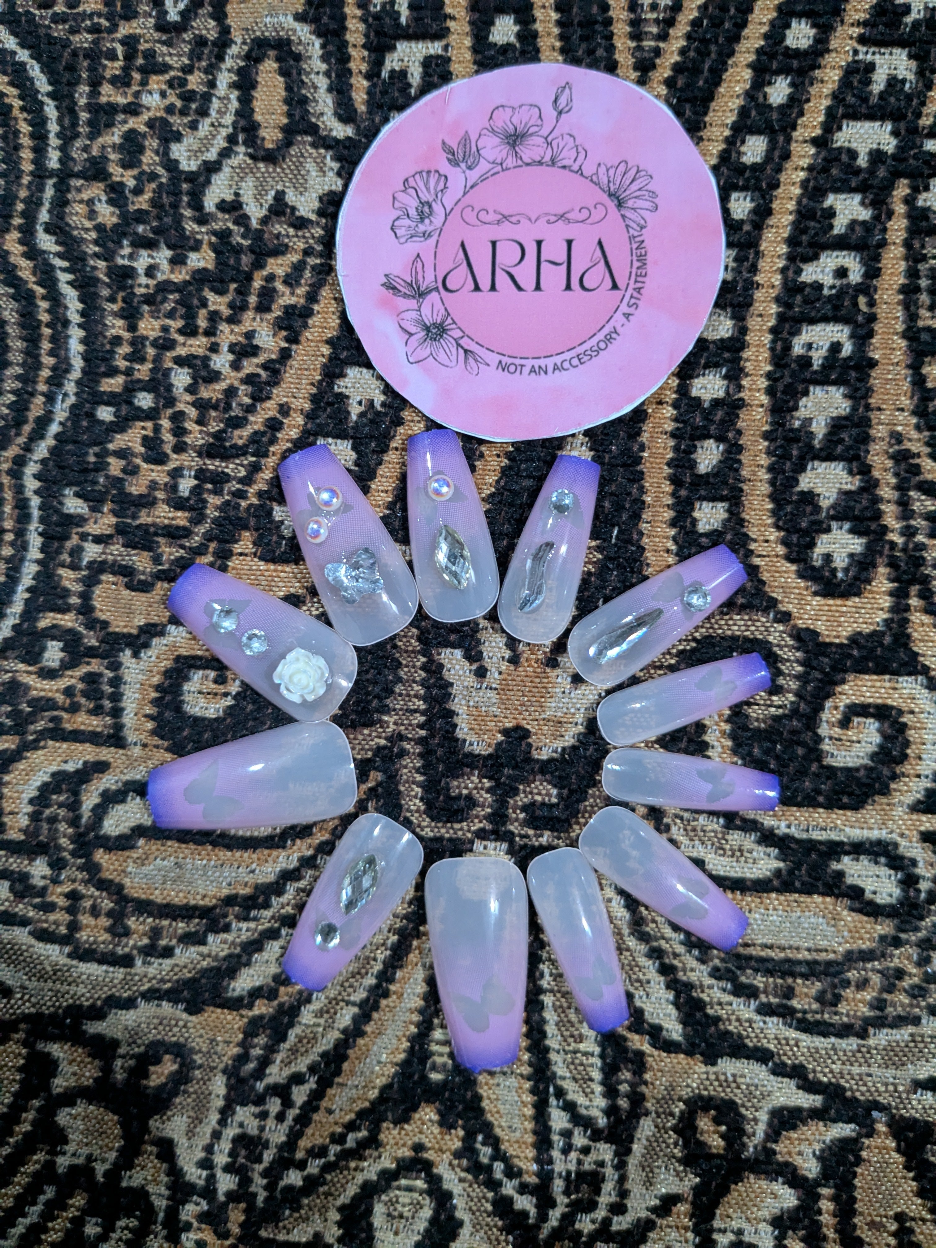 Set of purple and white nail extensions on a patterned fabric background