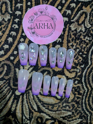 Set of purple and clear false nails with decorative elements on a patterned surface, featuring the brand 'ARHA'.