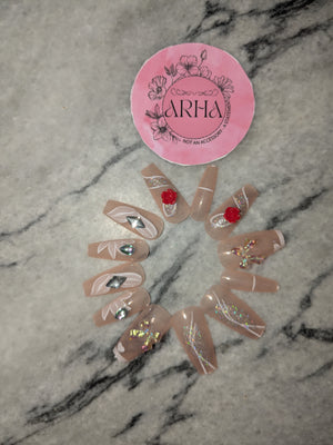 Set of decorative false nails with glitter and red accents on a marble surface with Arha brand logo.