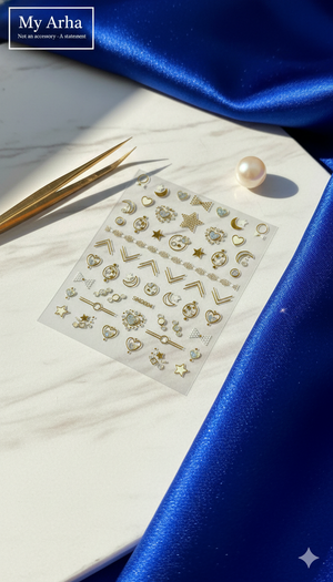 Professional flat lay of premium gold-foil nail art stickers with heart and celestial designs, featuring luxury gold tweezers and a pearl on a marble and blue silk background — My Arha DIY Beauty.