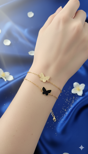 Hand wearing a gold bracelet with a butterfly charm on a blue fabric background